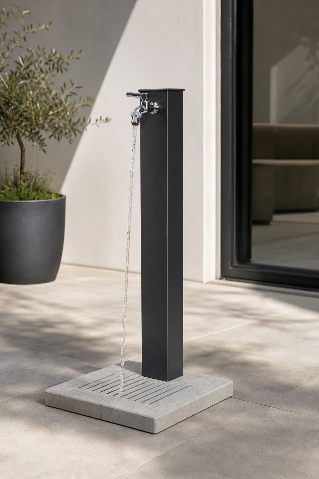 Fontaine de jardin en colonne Belfer anthracite en acier et aluminium avec socle en ciment, eau coulant du sommet, sur une terrasse en pierre contemporaine.